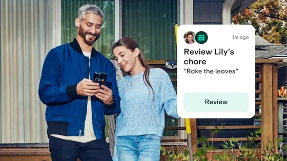 Father on a phone while his daughter looks at the phone with an overlayed graphic that says "Review Lily's chore" along with the description saying, "Rake the leaves" and a call-to-action "Review" button