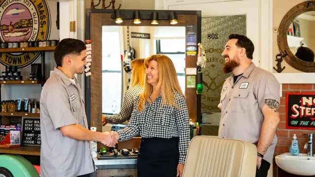 A North Easton Savings Bank lender shaking hands with a local business partner next to another local business partner inside of a barber shop