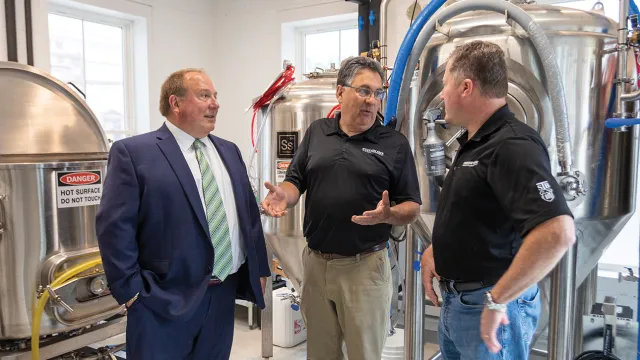 A North Easton Savings Bank lender standing and talking next to two local business partners in a brewhouse