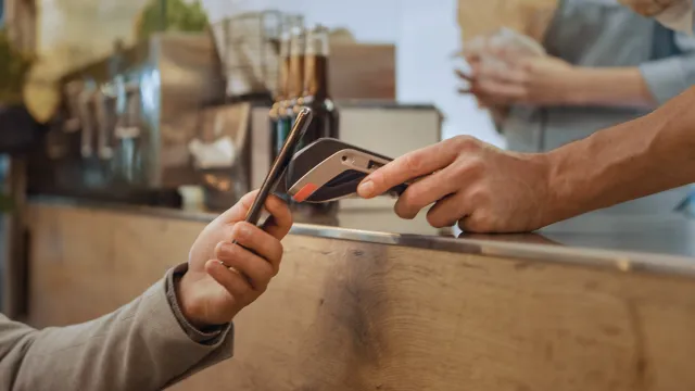 Person tapping their phone to a payment kiosk that is being held by an employee