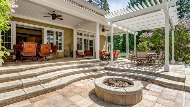 Backyard with a extensive hardscaping, a built-in stone fire pit, and a white pergola