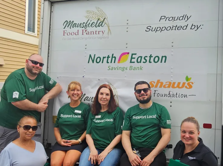Several North Easton Savings Bank employees wearing green "Support Local" t-shirts in front of a box truck for the Mansfield Food Pantry that has "Proudly Supported by North Easton Savings Bank" printed on the back door of the cargo box