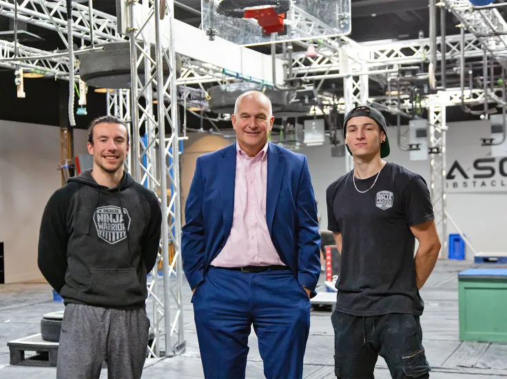 A North Easton Savings Bank lender standing next to two local business partners in a ninja warrior obstacle course gym space