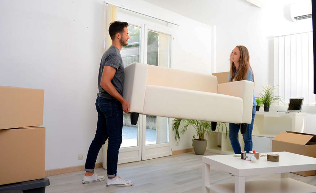 A young couple moving a large couch.